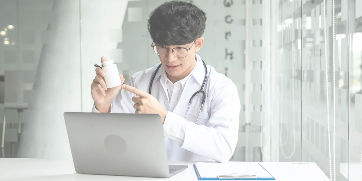 Doctor sitting in front of a laptop holding a medication box